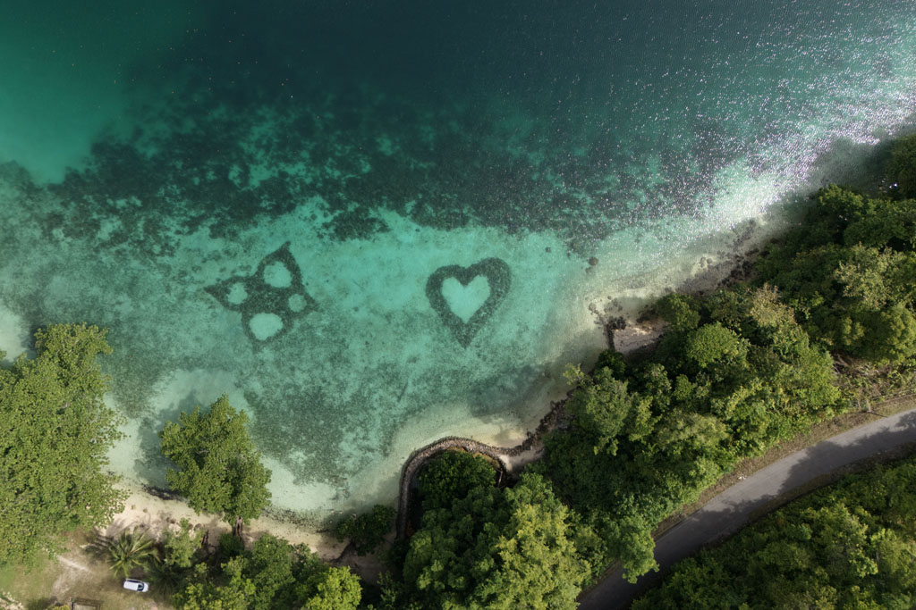Herz und Blumen Symbole aus Steinen im klaren Wasser am Teduang Beach