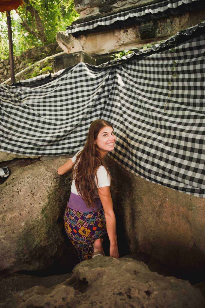 Junge Frau klettert in engen Hoehleneinstieg der Goa Giri Putri Cave