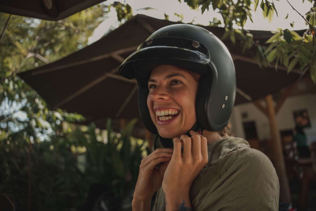 junge frau lacht und zieht helm an für rollerfahrt auf nusa penida
